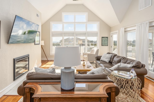 living area featuring light wood-type flooring, high vaulted ceiling, and visible vents