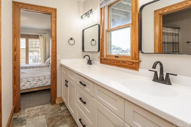 ensuite bathroom with stone finish floor, a sink, ensuite bath, and double vanity