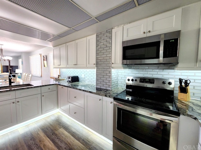 kitchen featuring stainless steel appliances, a sink, white cabinetry, light wood-type flooring, and dark stone counters