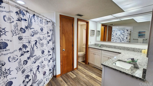 bathroom featuring a textured ceiling, toilet, wood finished floors, visible vents, and vanity