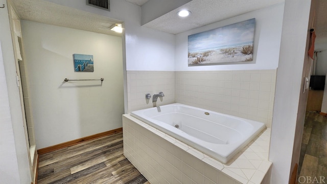 bathroom with baseboards, visible vents, a tub with jets, wood finished floors, and a textured ceiling