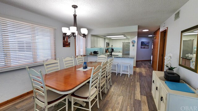 dining room with dark wood-type flooring, a notable chandelier, a textured ceiling, and baseboards