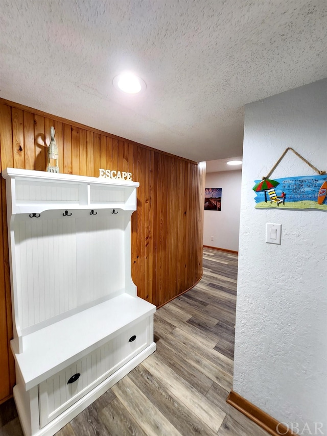 mudroom featuring a textured wall, wooden walls, a textured ceiling, wood finished floors, and baseboards