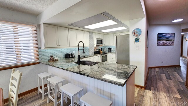 kitchen featuring stainless steel appliances, white cabinets, a sink, and a peninsula