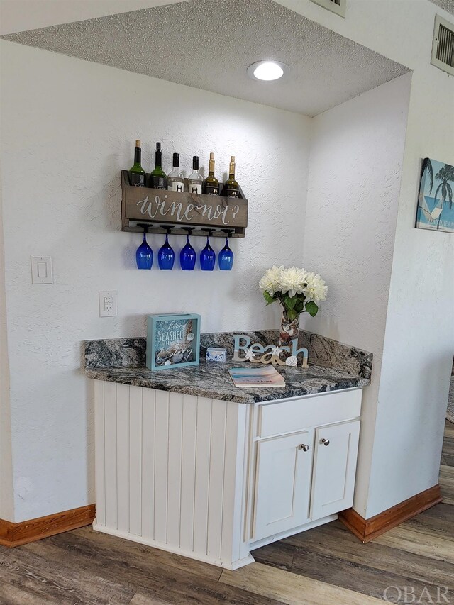 bar featuring a textured ceiling, a dry bar, dark wood-style flooring, and radiator