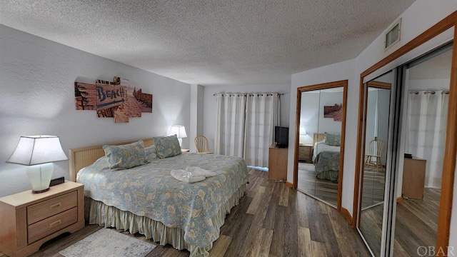 bedroom featuring a textured ceiling, dark wood finished floors, visible vents, and multiple closets