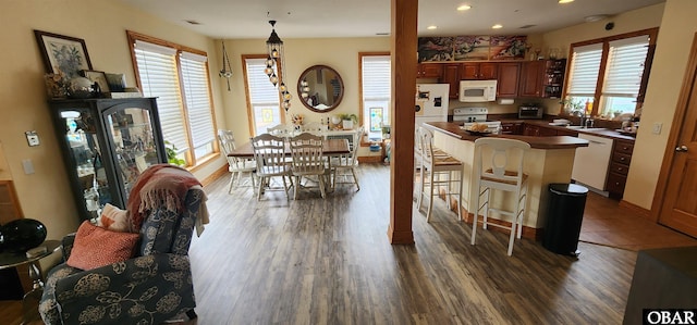 kitchen with a breakfast bar area, a peninsula, white appliances, a healthy amount of sunlight, and dark countertops