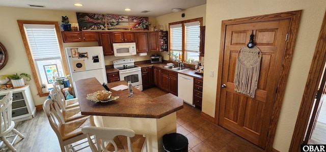 kitchen featuring a breakfast bar area, white appliances, a sink, visible vents, and tile patterned floors