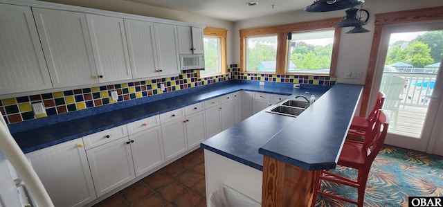 kitchen with dark countertops, white microwave, white cabinetry, and a sink