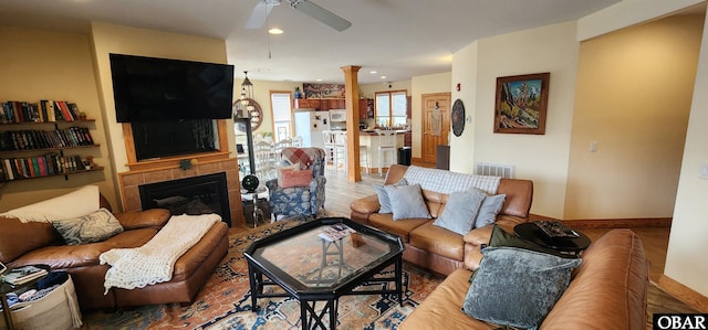 living area with ceiling fan, visible vents, baseboards, a tiled fireplace, and decorative columns