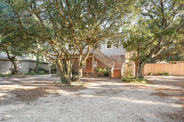 view of property hidden behind natural elements featuring driveway, stairs, fence, and board and batten siding