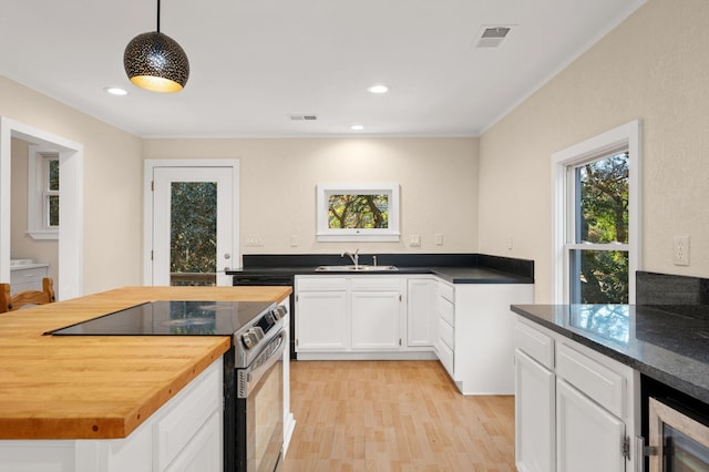 kitchen featuring electric range, butcher block counters, white cabinetry, hanging light fixtures, and a wealth of natural light