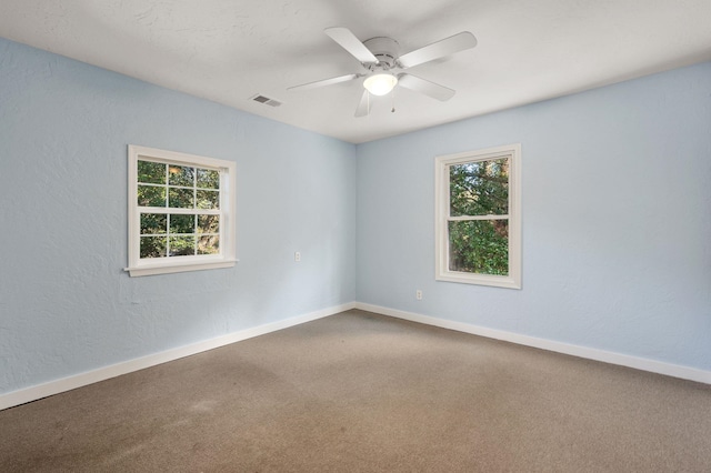 carpeted spare room with a textured wall, visible vents, ceiling fan, and baseboards