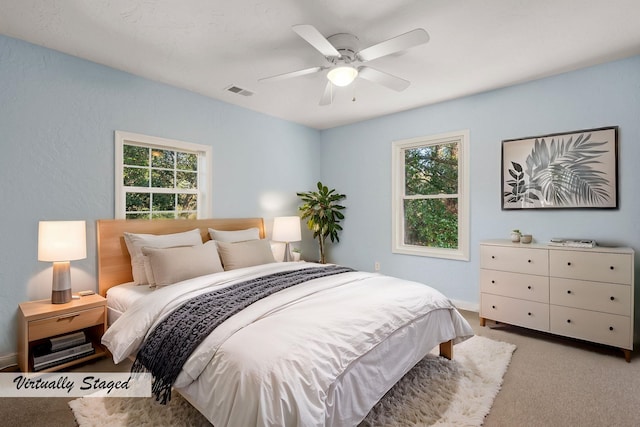 bedroom featuring multiple windows, visible vents, a ceiling fan, and light colored carpet