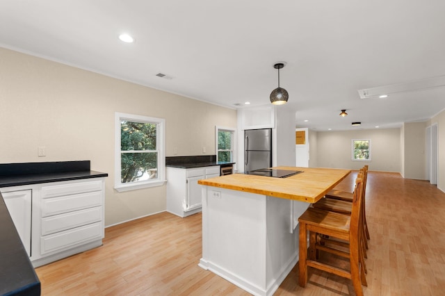 kitchen with hanging light fixtures, light wood finished floors, freestanding refrigerator, and white cabinets