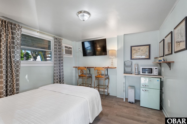 bedroom with a wall unit AC, baseboards, wood finished floors, and freestanding refrigerator