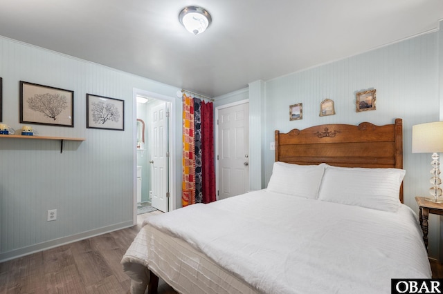 bedroom with ensuite bath, wood finished floors, and baseboards