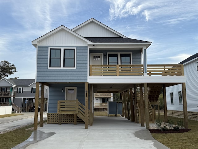 coastal inspired home with a carport, concrete driveway, roof with shingles, and board and batten siding