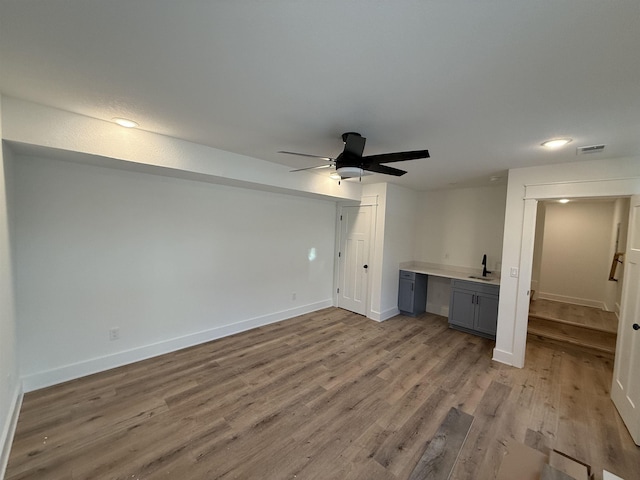 interior space featuring visible vents, light wood-style flooring, a ceiling fan, a sink, and baseboards