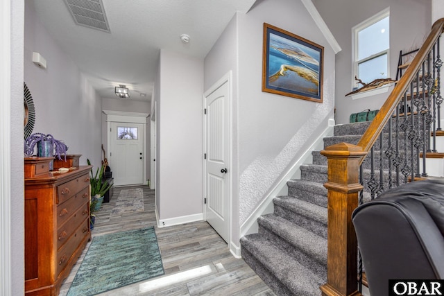 entrance foyer with light wood finished floors, visible vents, stairway, and baseboards