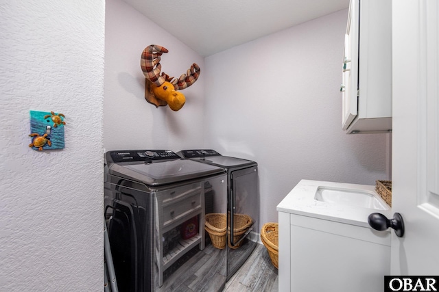 clothes washing area featuring light wood-type flooring, a textured wall, cabinet space, independent washer and dryer, and a sink