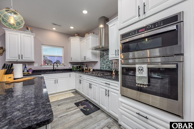 kitchen with light wood finished floors, white cabinets, stainless steel appliances, and wall chimney exhaust hood