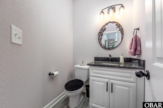 half bathroom featuring toilet, wood finished floors, baseboards, vanity, and a textured wall