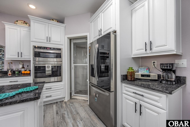 kitchen with light wood-style flooring, appliances with stainless steel finishes, white cabinets, and dark stone counters