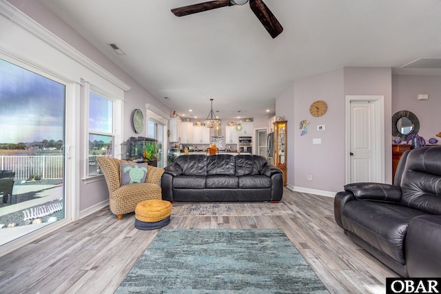 living room with visible vents, baseboards, light wood-style flooring, and ceiling fan with notable chandelier