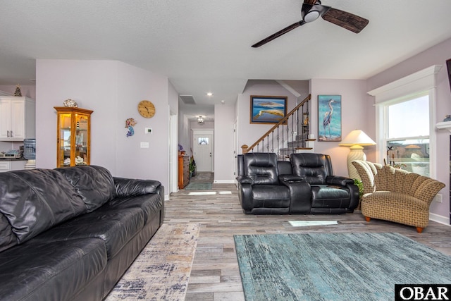 living room featuring visible vents, baseboards, light wood-type flooring, stairs, and a ceiling fan