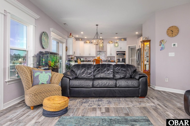 living room featuring recessed lighting, baseboards, light wood-style floors, and an inviting chandelier