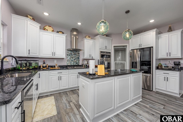 kitchen featuring stainless steel appliances, a sink, white cabinets, wall chimney range hood, and a center island