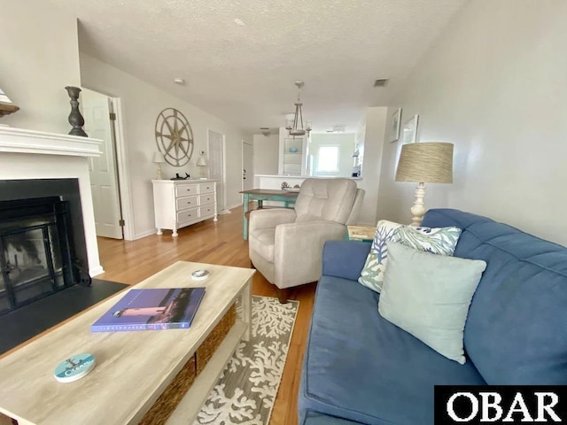 living area featuring a fireplace with flush hearth, a textured ceiling, visible vents, and wood finished floors