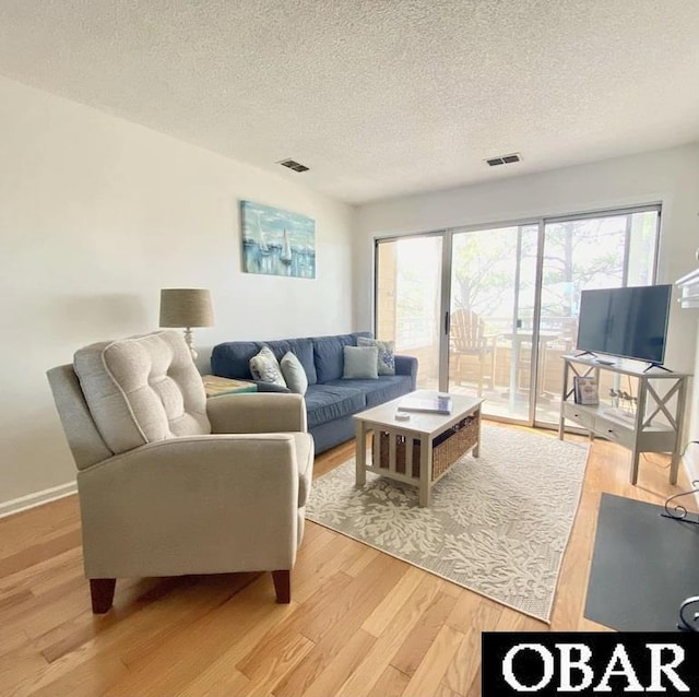 living room with a textured ceiling, a wealth of natural light, visible vents, and light wood-style floors