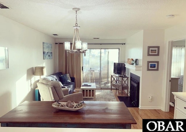 dining space featuring a fireplace with flush hearth, visible vents, a textured ceiling, and light wood finished floors