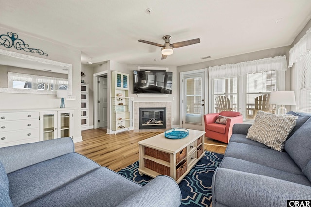 living room featuring a wealth of natural light, a tiled fireplace, and wood finished floors