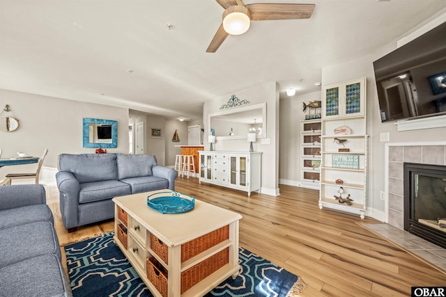 living area with wood finished floors, a tile fireplace, a ceiling fan, and baseboards