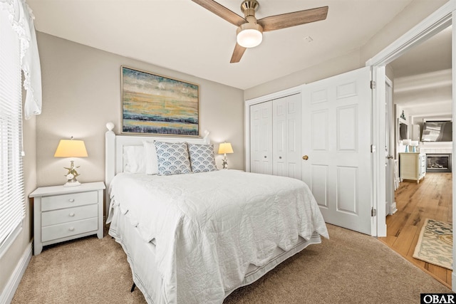 bedroom with light wood-type flooring, a closet, a fireplace, and ceiling fan