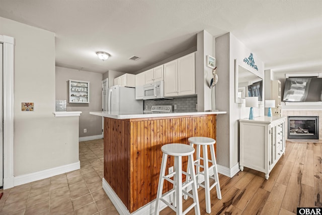 kitchen featuring white appliances, a breakfast bar, light countertops, white cabinetry, and backsplash