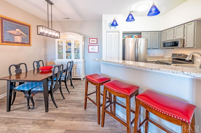 kitchen featuring pendant lighting, light wood finished floors, stainless steel appliances, gray cabinetry, and a sink