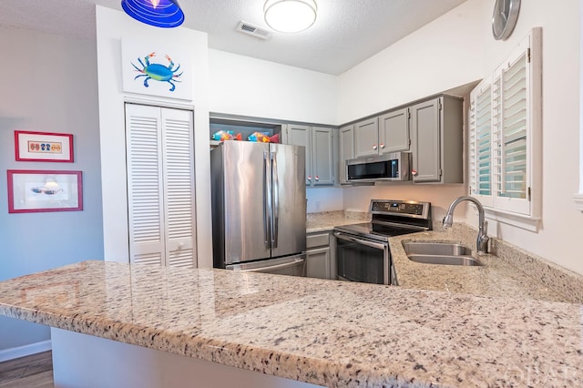 kitchen with a textured ceiling, a peninsula, a sink, visible vents, and appliances with stainless steel finishes