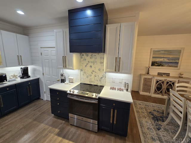 kitchen featuring dark wood-type flooring, ventilation hood, light countertops, stainless steel range with electric stovetop, and white cabinetry