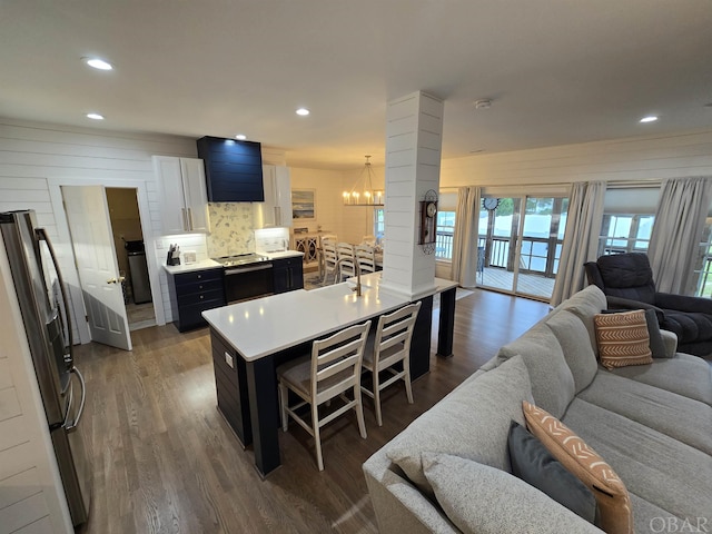 kitchen with a kitchen island with sink, white cabinetry, light countertops, freestanding refrigerator, and a kitchen bar