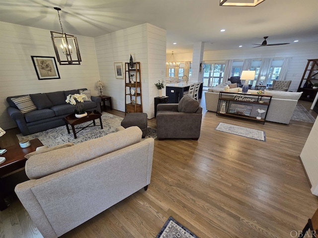 living area with ceiling fan with notable chandelier, dark wood finished floors, and recessed lighting