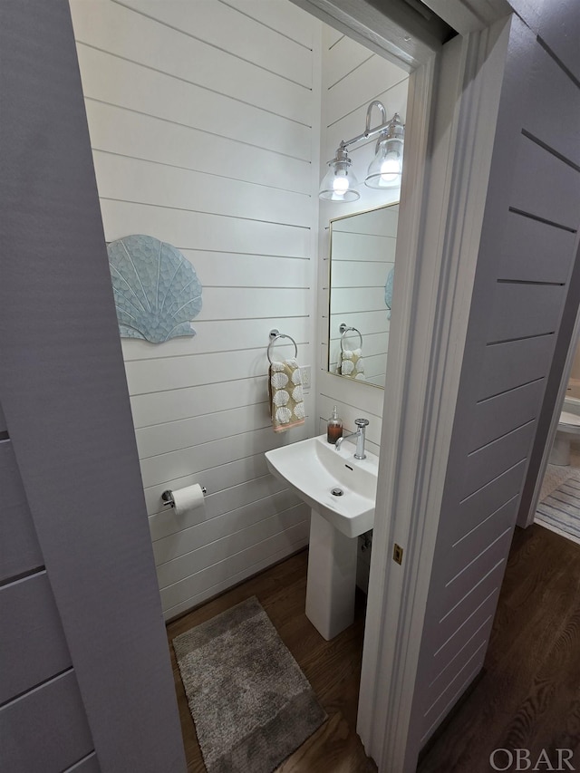 half bathroom with wood walls and wood finished floors