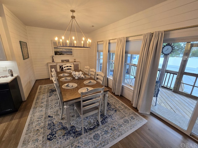 dining room with dark wood-style floors, wooden walls, and a chandelier