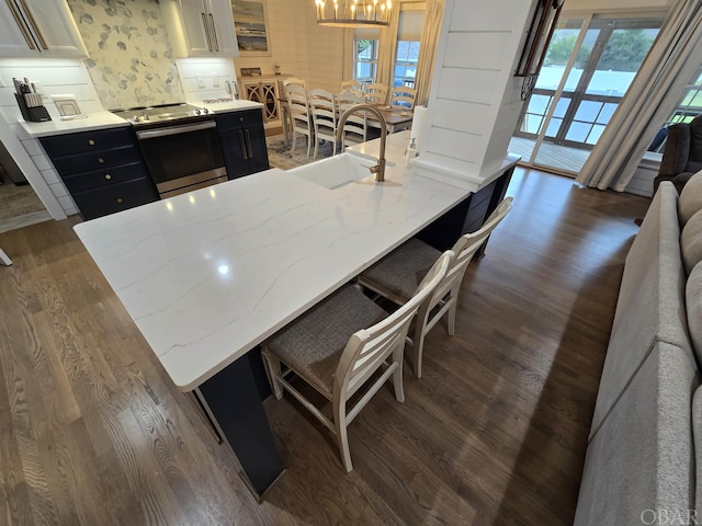 kitchen with electric stove, a kitchen breakfast bar, dark cabinetry, white cabinetry, and a sink