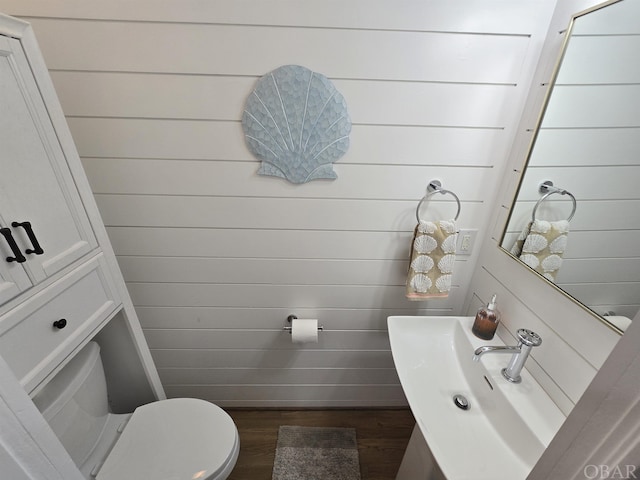 bathroom with a sink, wood walls, toilet, and wood finished floors