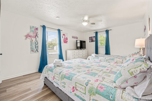 bedroom with light wood-style flooring, multiple windows, baseboards, and a textured ceiling