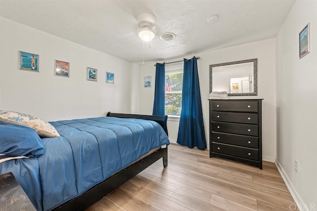 bedroom with a textured ceiling, ceiling fan, baseboards, and light wood-style floors